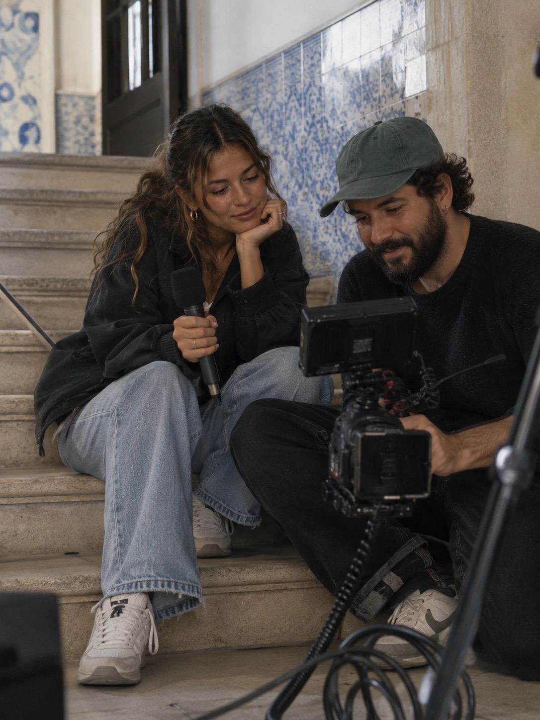 A creator and a video editor reviewing footage on the steps of a tiled stairwell